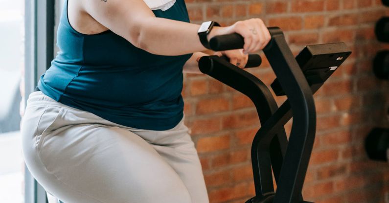 Motivation Stagnation - Side view of cheerful plus size ethnic female in activewear with towel exercising on fitness equipment during workout in gym