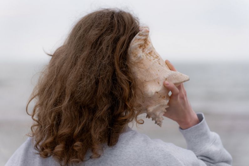 Deep Listening - a woman with long hair holding a seashell up to her face