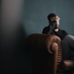 Emotions Decision - a man holds his head while sitting on a sofa