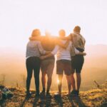 Social Support - four person hands wrap around shoulders while looking at sunset