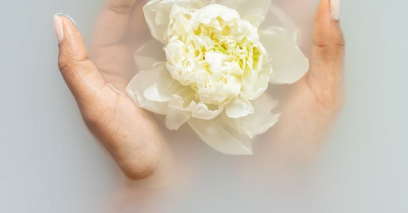 Nature Therapy - Unrecognizable female with soft manicured hands holding white flower with delicate petals in hands during spa procedures