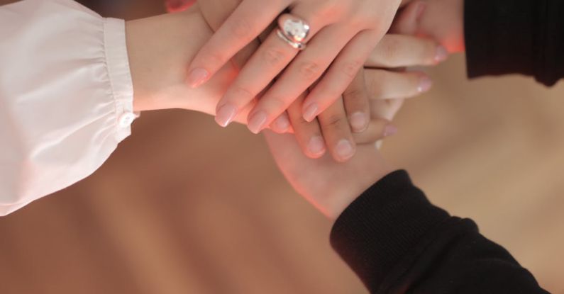 Supportive Community - Top view of faceless friends in different clothes stacking hands together while standing on wooden floor indoor on sunny day
